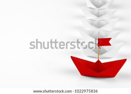 Close up red paper ship leader among white ships. Business and leadership concept. Isolated on white background. Paper craft and origami. 