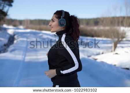 Redhead girl with black track suit standing on the snow. Profile photo. 