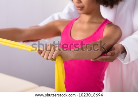 Physiotherapist Assisting Woman While Exercising With Exercise Band Royalty-Free Stock Photo #1023018694