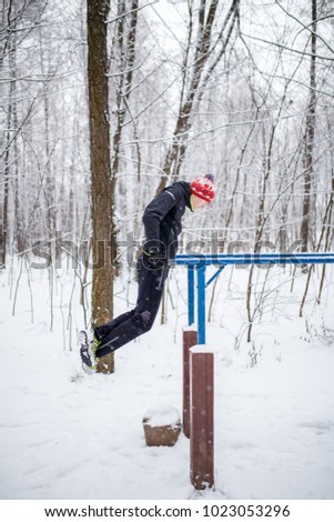 Image of sports man on horizontal bar in winter at woods