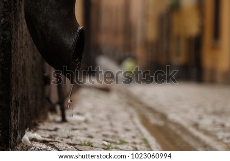 Closeup of black steel drain pipe on background of cobbled street, closeup of water drops splashing out from pipe