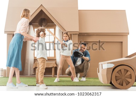young family playing baseball together on yard of cardboard house isolated on white