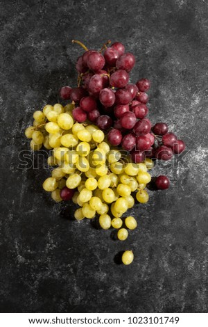 White and red bunch of grapes on a black worn background.
