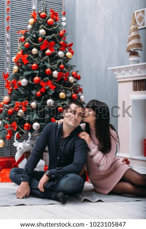 Lovely happy young couple poses before a red Christmas tree in a cosy corner