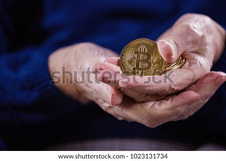 Closeup of senior woman with couple of bitcoins, demonstrating one of them.