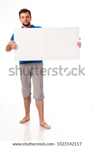 A guy with a beard posing with a white sign. Shows different emotions. Isolated on a white background. In a gray trousers and a blue T-shirt. For advertising, logo, business cards, contact phones, etc