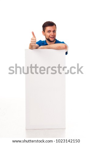 A guy with a beard posing with a white sign. Shows different emotions. Isolated on a white background. In a gray trousers and a blue T-shirt. For advertising, logo, business cards, contact phones, etc
