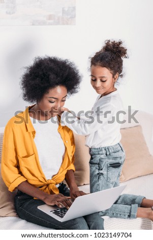 african american mother and daughter looking at laptop at home 