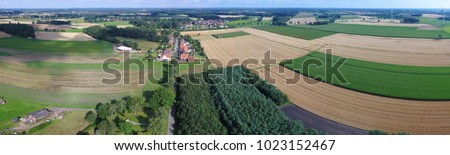 Aerial view of fields, meadows and forests with a street in the middle and a small village in the background, landscape