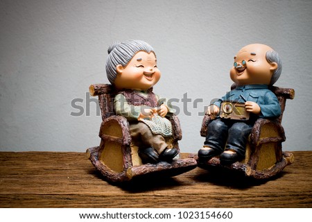 still life photo style of lovely chinese grandparent doll siting rocking bamboo chair on wooden table with gray concrete wall. Chinese New Year & Love concept. light painting photography.
