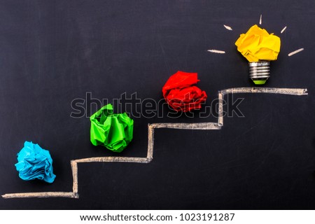 Evolving idea concept with colorful crumpled paper and light bulb on steps drawn on blackboard. Royalty-Free Stock Photo #1023191287