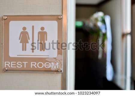 Brown restroom sign with word "REST ROOM" hanging on soft brown wall in front of entrance 