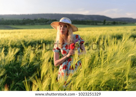 Cute girl in a straw hat in a dress in a wheat field at sunset, a smile on her face