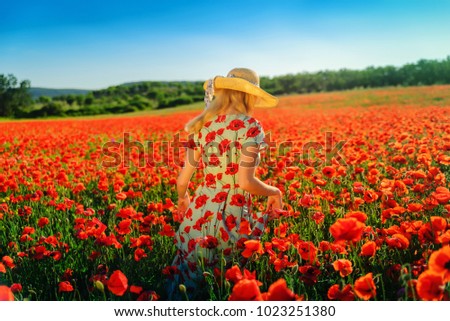 Cute girl in a straw hat in a blooming field of red poppies, positive emotions, gorgeous flowers, leaves in the sunset