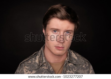 Cheerless young veteran looking at camera with upset look. He is feeling hopeless and loneliness. Isolated on black background