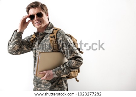 Joyful young male officer going and setting straight his spectacles. He is smiling and holding document case. Isolated on background. Copy space in right side