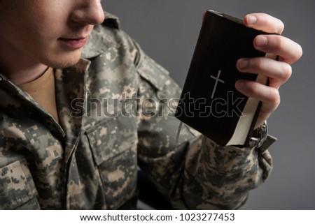 military man holding the book in his hand. He is wearing military uniform. Focus on close up of his hand with book. Isolated on grey background
