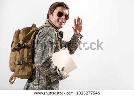 Cheerful military guy waving his hand and smiling. He is looking at camera while going away. Isolated on background. Copy space in right side