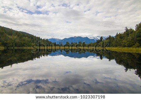 Peaceful landscape of natural calm water mirror reflecting the cloudy sky, mountains, hills and forest, Lake Matheson in West Coast, Fox Glacier, New Zealand