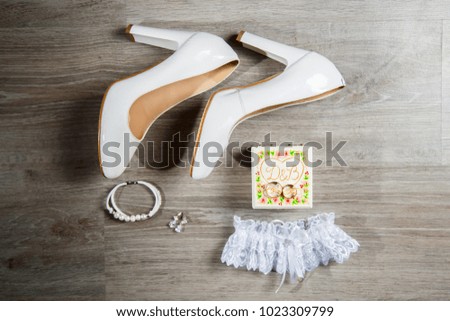 White bride shoes on a wooden floor with earrings, perfume and garter