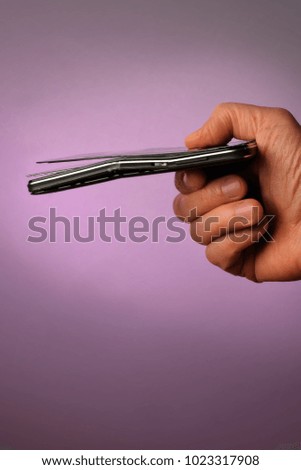 broken black mobile smartphone with a cracked display lying in his hand, on a lilac background,, side view