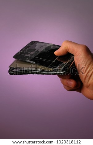 broken black mobile smartphone with a cracked display lying in his hand, on a lilac background
