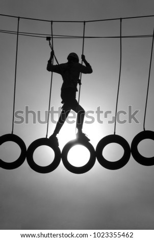 silhouette of a climber fastened and standing on used car tires in an adventure park