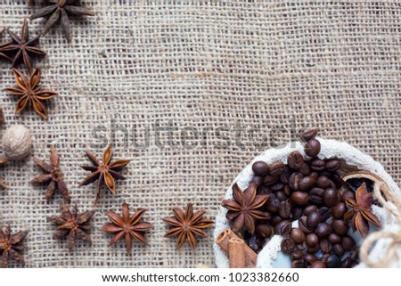 A lot of coffee bean in cup with cinnamon, anis-star, on sackcloth.