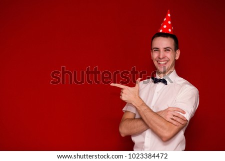 Happy man a white shirt a red cap pointing finger and looking in camera. Photo for business projects, product presentation. Image with copy space isolated on red