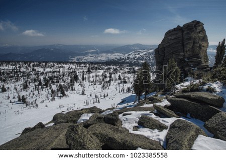 Big stone rocks above winter snow mountains under clear sky