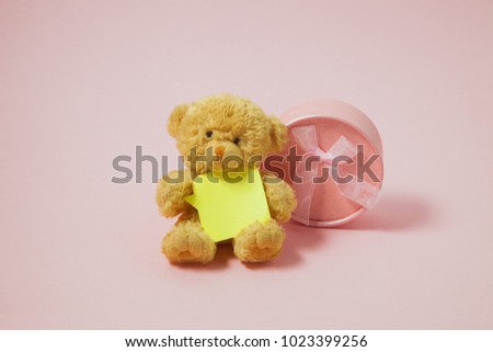 A small toy teddy bear with an empty blank and gifts on a light background. The concept of a greeting card for Valentine's Day, mother's day, birthday.