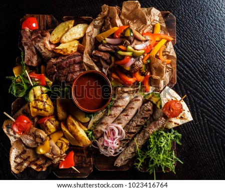 Assorted delicious grilled meat with vegetable. Mixed grilled bbq meat with vegetables. Mixed grilled meat on wooden platter. Top view. Royalty-Free Stock Photo #1023416764