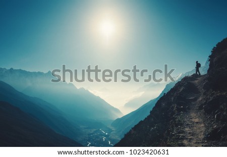 Standing woman on the hill against mountain valley at bright sunny day. Landscape with girl, trail, mountain, blue sky with sun and low clouds at sunset in Nepal.  Lifestyle, travel. Trekking Royalty-Free Stock Photo #1023420631