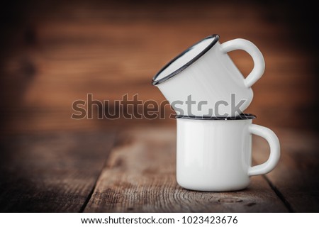 Two enameled cups on wooden rustic kitchen table. Royalty-Free Stock Photo #1023423676