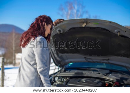 Redhead girl standing in front of broken car. Close-up shot.