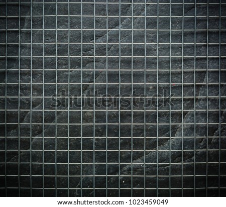 Metal mesh on black stone wall background in the dark.