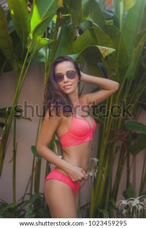 attractive young woman in bikini in front of tropical leaves in garden