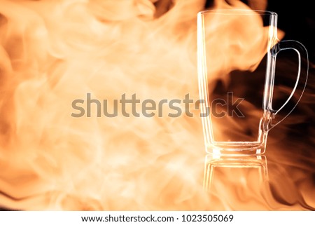 En empty beer mug isolated on a black background in the fire flames.