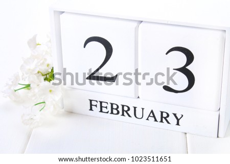White wooden calendar with black 23 february word with clock and plant on white wood table