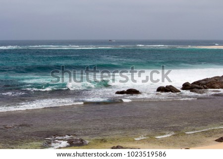 Tide ebbing out from the  famous white sandy  surfing beach and rocky shore  at Margaret River South Western Australia  on a calm cloudy afternoon in  early summer  creates a scenic seascape.
