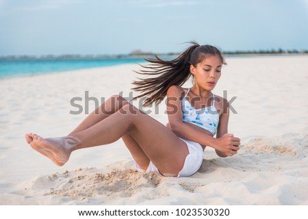 Abs workout - fitness woman working out on beach doing russian twists abs exercises with raised legs for stomach weight loss toning. Fit body oblique muscles training Asian girl. Royalty-Free Stock Photo #1023530320