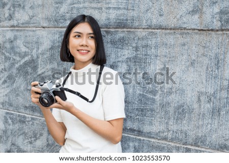 Attractive Asian woman holding retro camera with smiling, Woman using camera at outdoor place.