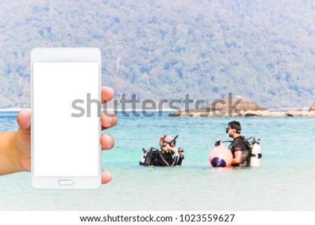 Man use mobile phone, blur image of diving class in the sea as background.