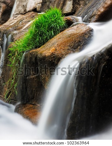 Giant boulders of a stream create a waterfall with mimicking falling grass. Creamy textures created by  time lapse photography make water silky smooth.
