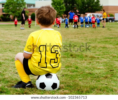 Young boy child in uniform watching organized youth soccer or football game from sidelines Royalty-Free Stock Photo #102365713