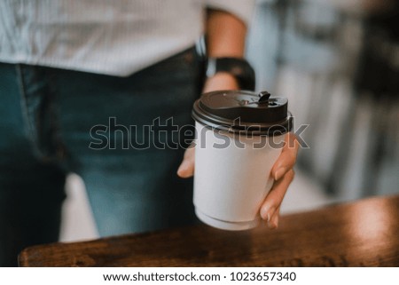 Hand in blue shirt is holding a white paper cup