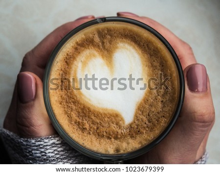 the girl is holding a cup of coffee with a heart of foam Royalty-Free Stock Photo #1023679399