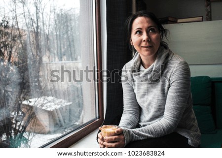 the girl is holding a cup of coffee near the window and talking
