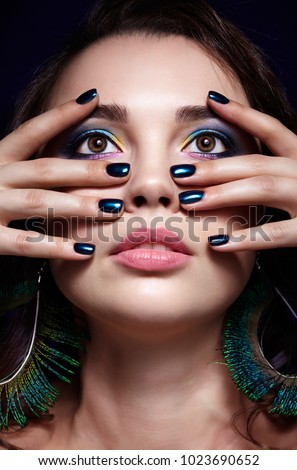 Portrait of beautiful brunette woman on black background. Female with blue eye shadow make up and manicure. Girl with peacock feather earrings
