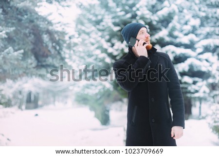 Man calls on mobile phone in the snow-covered pine forest on a cold winter day